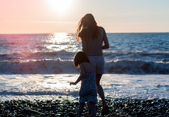 Mother with child girl at the sea beach on sunset