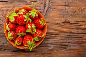 Ripe strawberries in a clay plate on a dark wooden surface.