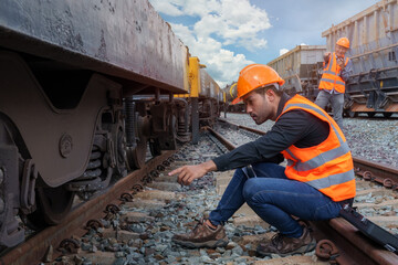 Two engineers point focus to train wheels, and senior engineer use walkie talkie on freight train...