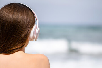 Alone woman on a beach in headphones listen music looking on the sea. Female relaxation at summer vacation. Back view