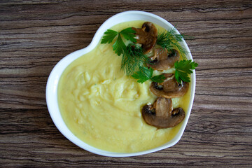 Mashed potatoes. A garnish of champignon mushrooms with mashed potatoes are in a white heart-shaped plate. View from above.