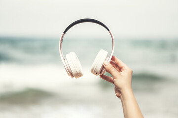 Woman hands with headphones on a beach and sea coastline.