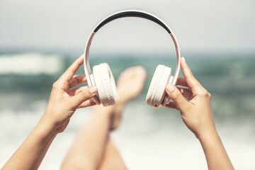 Woman hands with headphones on a beach and sea coastline.