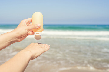 Woman applying sunscreen on skin of hand on a beach of coastline sea. Female relaxation at summer vacation. Back view