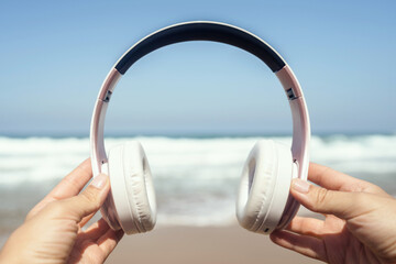 Woman hands with headphones on a beach and sea coastline.