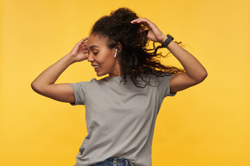 young happy african american wears grey t-shirt dancing while listening good music via headphones. isolated over yellow background.