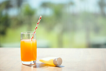 Sunscreen for protection skin and orange juice on the table in the palm tree forest. Summer vocation.