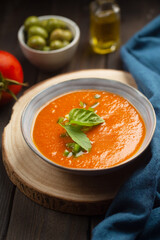 traditional spanish dish gazpacho with green leaves on a dark wooden table