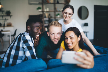 Glad multiethnic partners taking selfie on smartphone on sofa