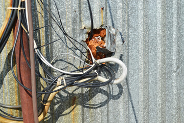 A lot of tangled wires, cables are connected to each other, carelessly come out of a galvanized...
