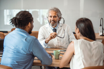 Male doctor consulting with young couple in doctor's room. Male doctor explaining diagnosis to a...