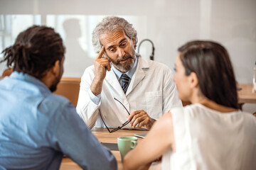 Obraz premium Cropped shot of a young couple having a consultation with their doctor. Shot of a doctor having a consultation with a couple in a clinic. Young couple during the consultations at clinic.
