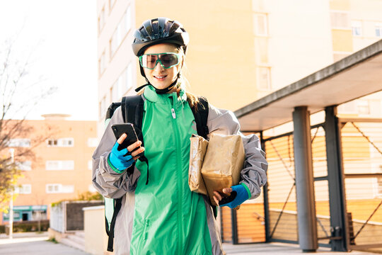 Female courier with parcels using smartphone