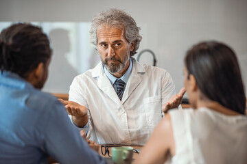 Senior healthcare worker discussing with couple. Male doctor is showing digital tablet to man and woman. They are sitting in hospital. Consultation In Doctors Office