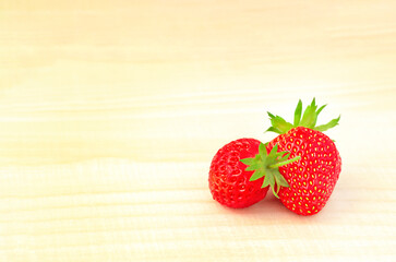 Two red strawberries lie on a wooden background