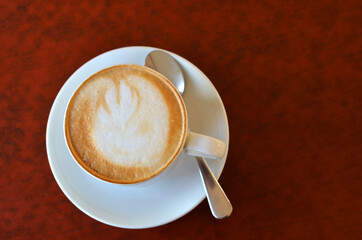 cup of cappuccino with foam in a white porcelain mug with a spoon on a burgundy table