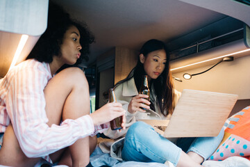 Diverse girlfriends using laptop in camper van
