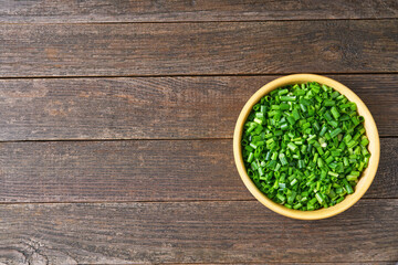 fresh green onions in a wooden bowl on the table, top view.