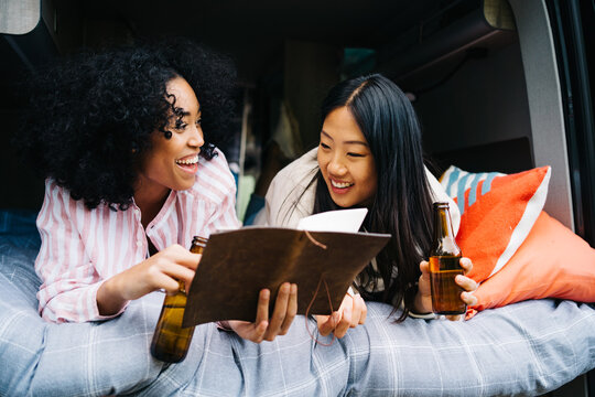 Happy diverse girlfriends with beer reading map in camper van