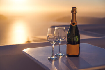Romantic evening on Santorini. Couple of glasses and bottle of champagne on white table. VIew of sunset under caldera. Close-up.