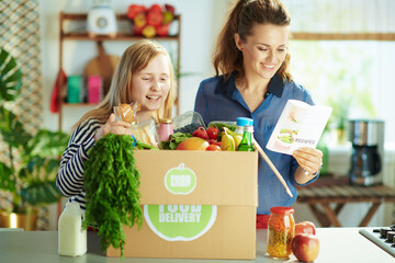 happy modern mother and daughter with food box in kitchen