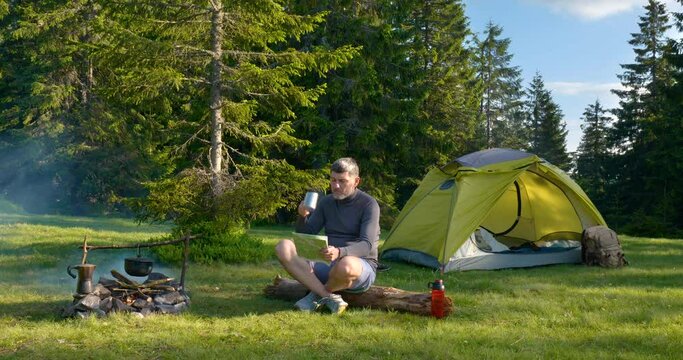 The man drinks tea and looks at the map in the Camping.