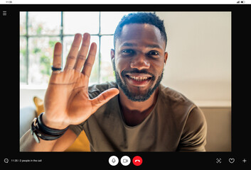 Young man saying hello to someone while having a video call at home. © Mego-studio