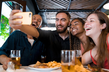 Group of friends taking a selfie with a mobile phone at a restaurant.