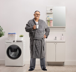 Obraz premium Man wearing a robe and standing inside a bathroom with a cup of coffee