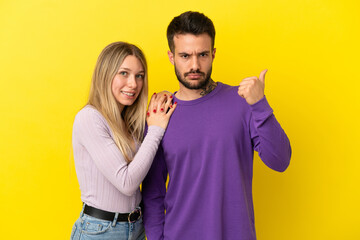 Obraz premium Young couple over isolated yellow background frustrated and pointing finger to the side
