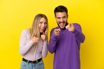 Fototapeta premium Young couple over isolated yellow background points finger at you