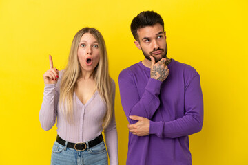 Young couple over isolated yellow background standing and thinking an idea