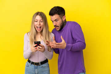 Naklejka premium Young couple over isolated yellow background sending a message or email with the mobile