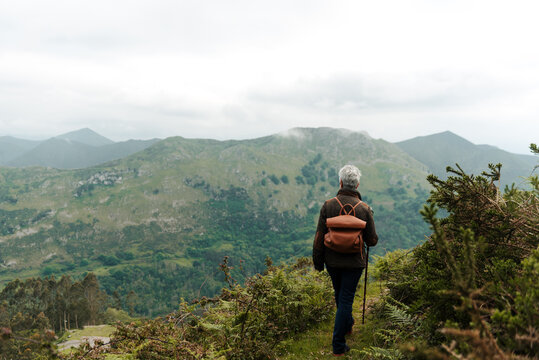 Unrecognizable senior female traveler walking towards mountain