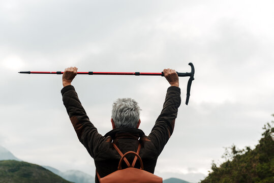 Unrecognizable elderly female hiker raising walking stick over head