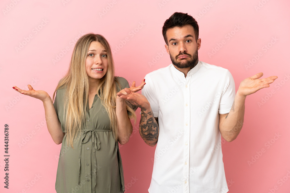 Wall mural Pregnant woman and man over isolated pink background having doubts and with confuse face expression