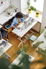 African-American woman designer looks at drawing by sewing machine shooting video in studio
