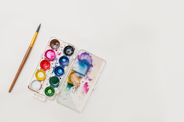 colored watercolor paints with a palette and a brush for drawing on a white background copy the...