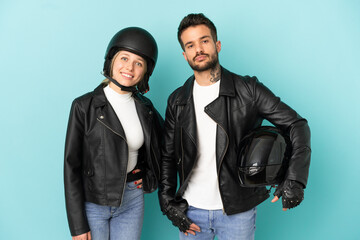 Couple with motorcycle helmet over isolated blue background posing with arms at hip and smiling