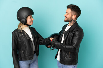 Couple with motorcycle helmet over isolated blue background handshaking after good deal