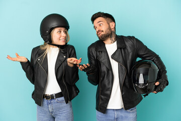 Couple with motorcycle helmet over isolated blue background making unimportant gesture while lifting the shoulders