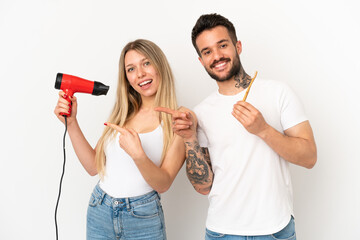 Couple holding a hairdryer and brushing teeth over isolated white background pointing finger to the...