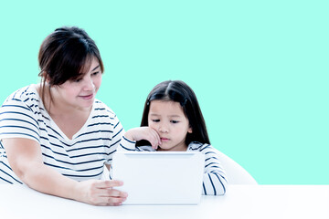 An Asian middle-aged mother and her 6 year old daughter is looking at the  tablets for online learning, On green soft isolated background, to children education online concept.