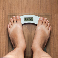 Top view of barefoot male standing on digital scale for weight control on wooden floor. First-person view. Slimming concept. Diet concept. Health concept.
