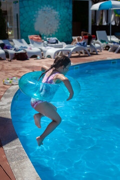 levitation concept, a girl in a pink swimsuit and a blue inflatable circle jumps into the water from a diving board in a hotel on a family vacation. 