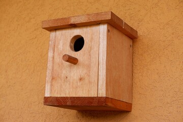 brown color natural wooden bird feeder nest on yellow house wall