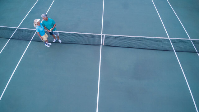 Overhead View Of Senior Couple Playing Tennis On Sunny Day.