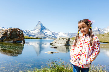 Naklejka premium Cute little girl outdoors in the lawn and admiring mountains view in mountain in switzerland