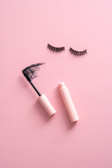 Flat lay mascara with stroke and false eyelashes on pink background.