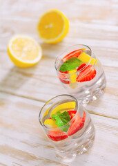 refreshing cocktail in two glasses on a light wooden table next to lemons. summer drink made from lemon, strawberry and mint.